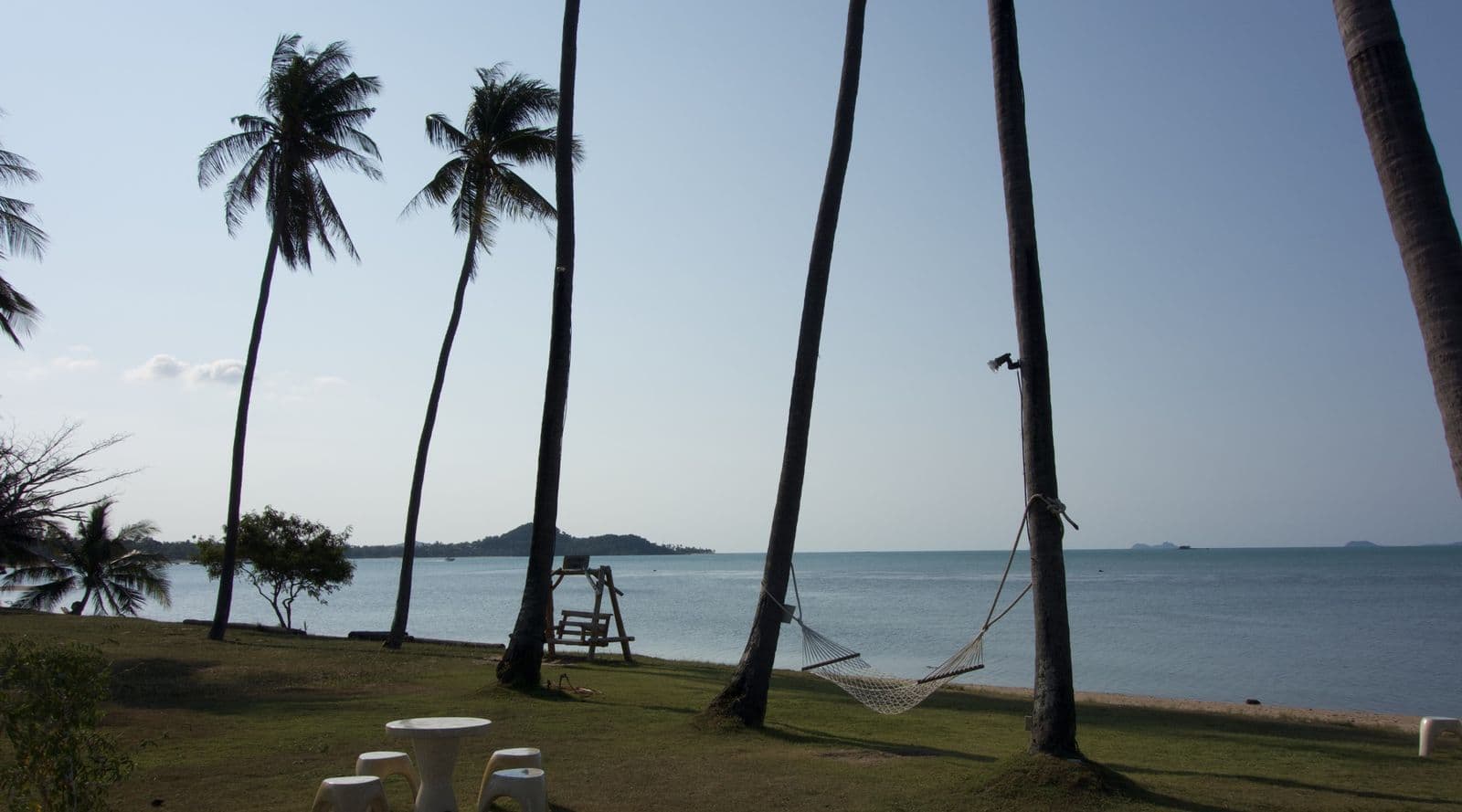 Tall coconut palms and a hammock on a lawn above a calm sea and distant islands