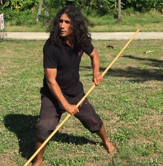 A student in a low stance with a bamboo staff on a grass field