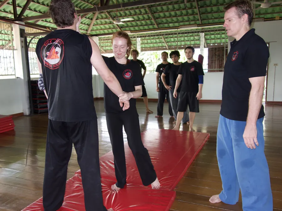 Rick Tew coaches a woman through a wrist-grab release while the class waits