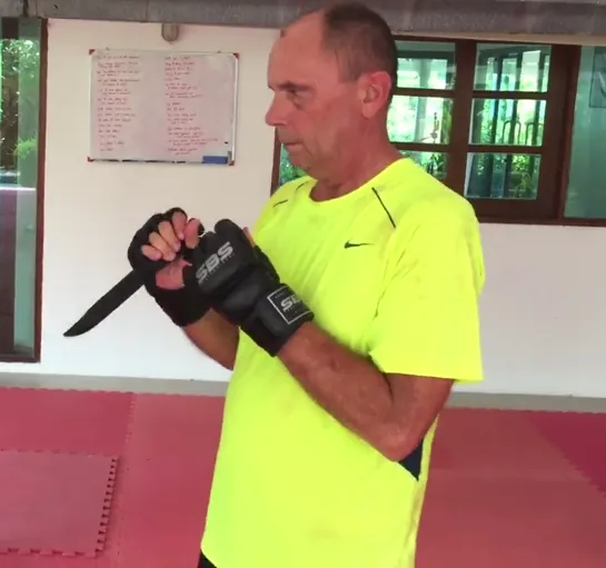 An older student in a yellow shirt holds a training knife