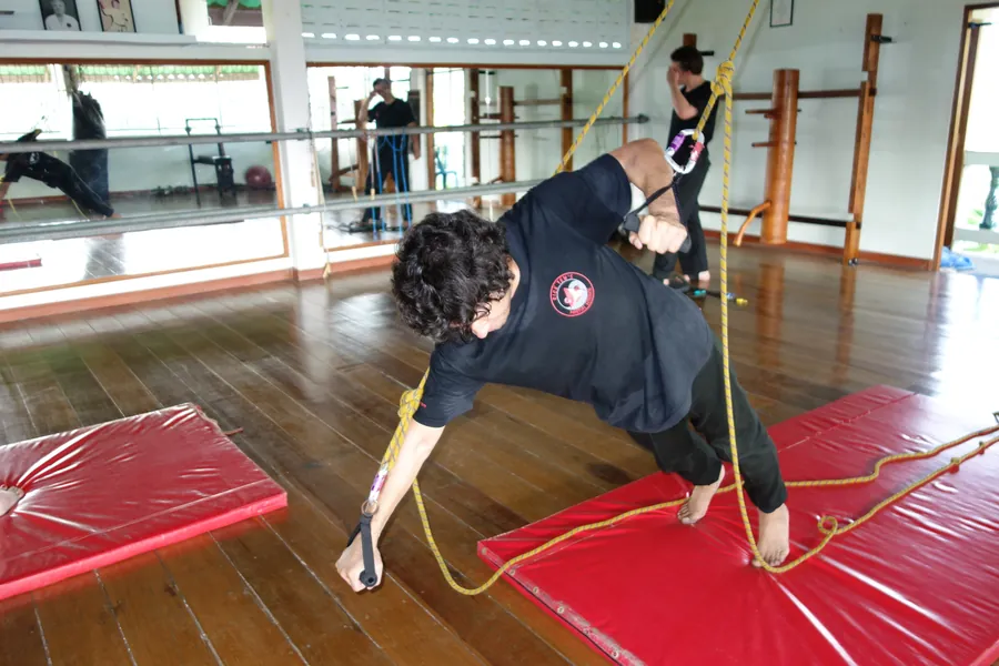 A student stretches low on a red mat with a rope, in an open-air hall