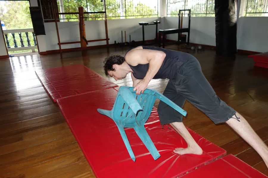 A student practices a roll over a plastic chair on the red mats