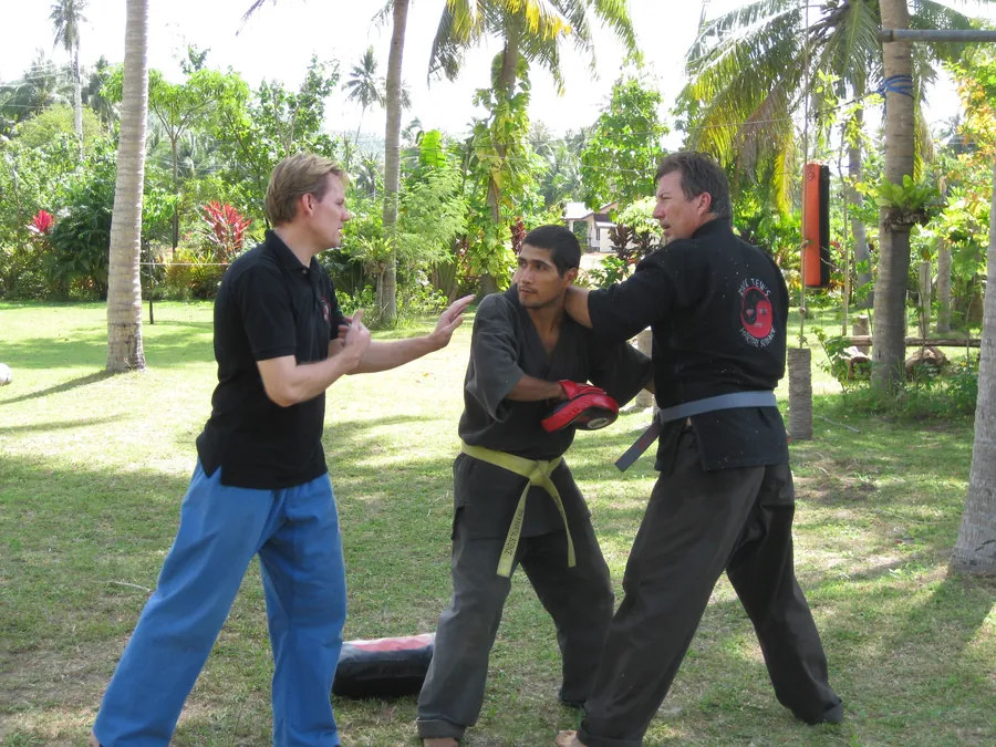 Rick Tew coaches two students through an arm block on a palm-garden lawn