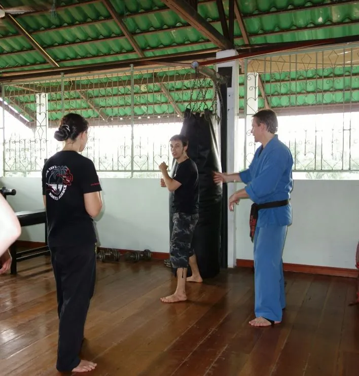 Rick Tew in a blue uniform watches two students drill in an open-air hall