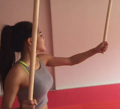 A woman raises a stick to block on a red mat