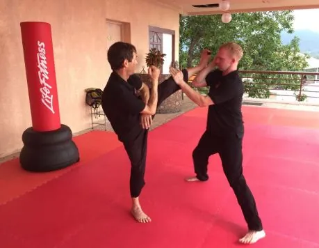 Two students drill a kick and a block on red mats by an open balcony