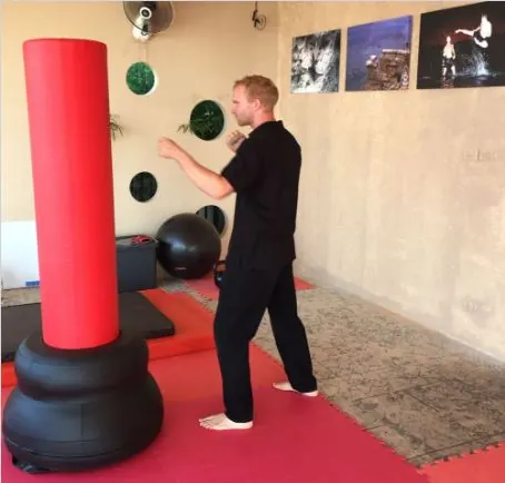 Rick Tew squares up to a red standing bag, three photos on the wall behind him