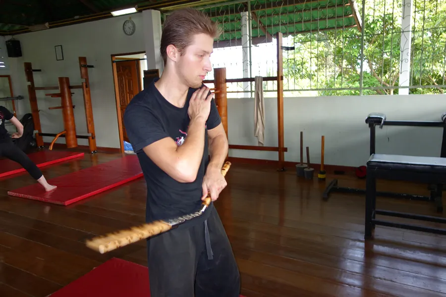 A student trains with nunchaku in an open-air hall