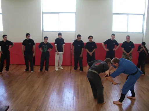 Rick Tew in a blue uniform shows a takedown while a line of students watches