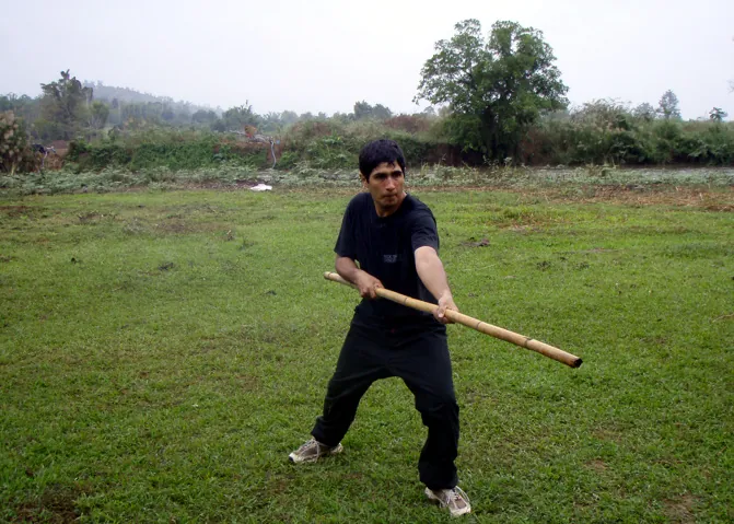 A student swings a long staff on an open field