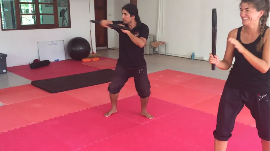 Two students face off with training sticks on pink mats