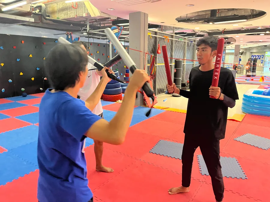 Students drill with padded sticks in a bright gym