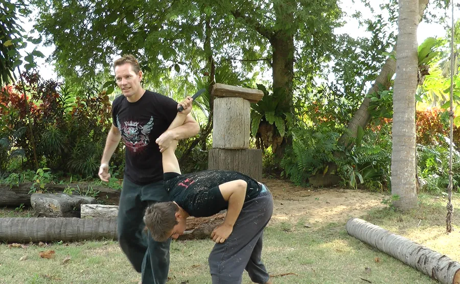 Rick Tew, smiling, takes a student's arm into a lock in a tropical garden