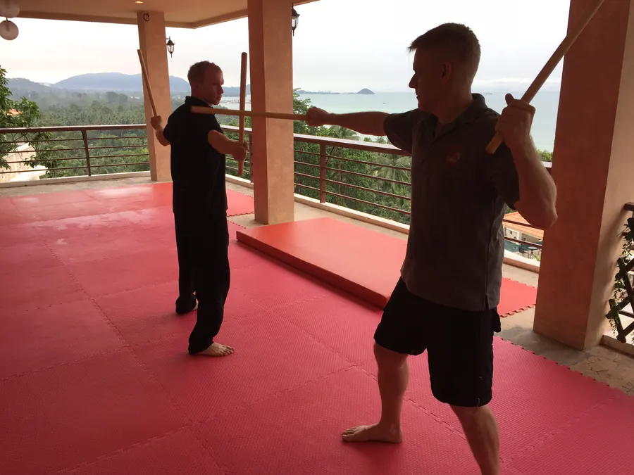Rick Tew works the long staff with a student on a terrace above the sea