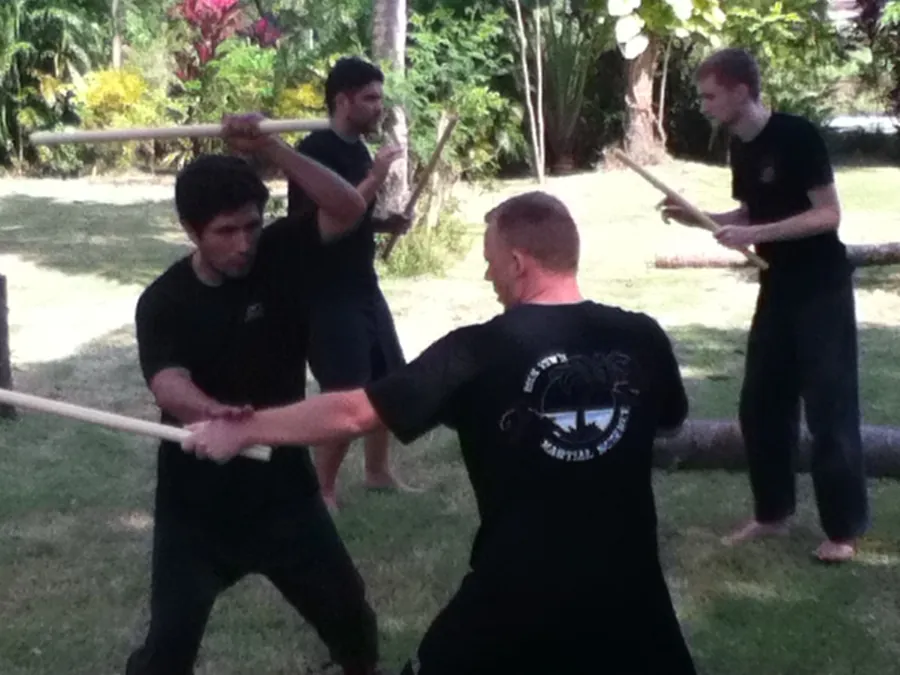 A student blocks a stick strike with his own stick on a garden lawn