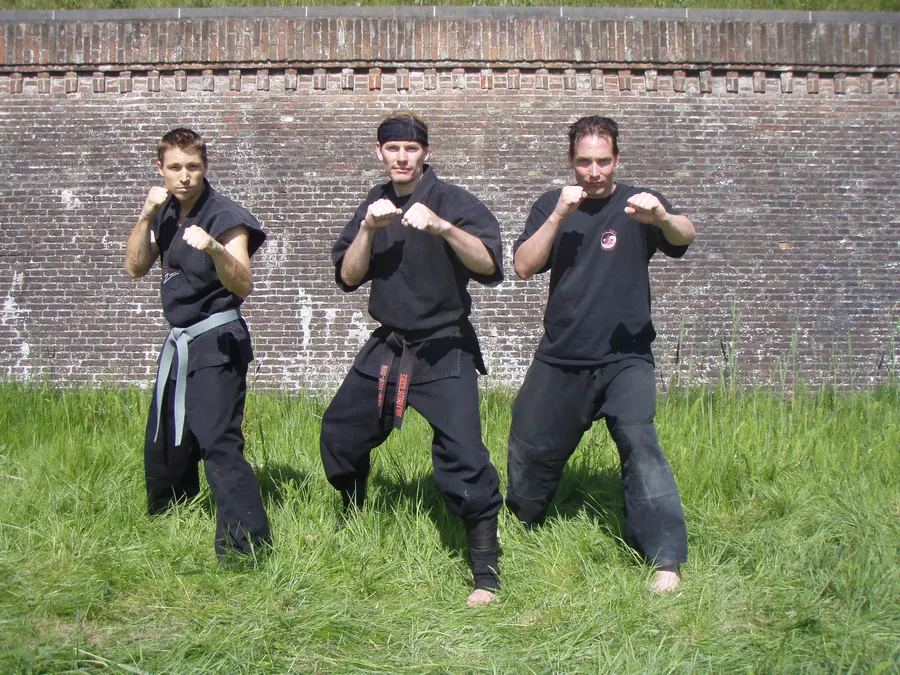 Three students in guard stance in front of an old brick fortress wall