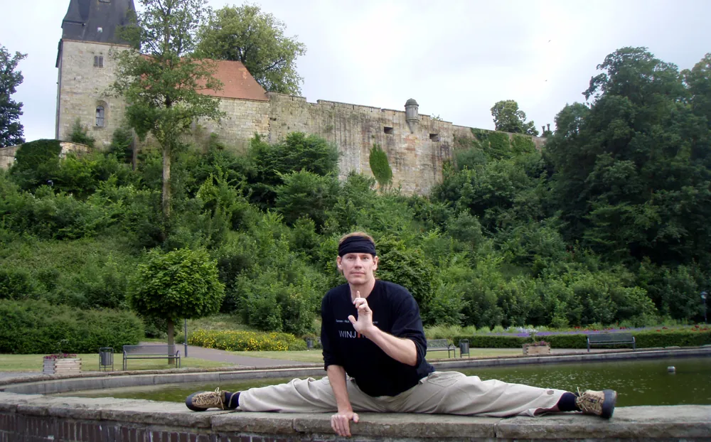 Rick Tew in the splits on a low wall in front of a castle