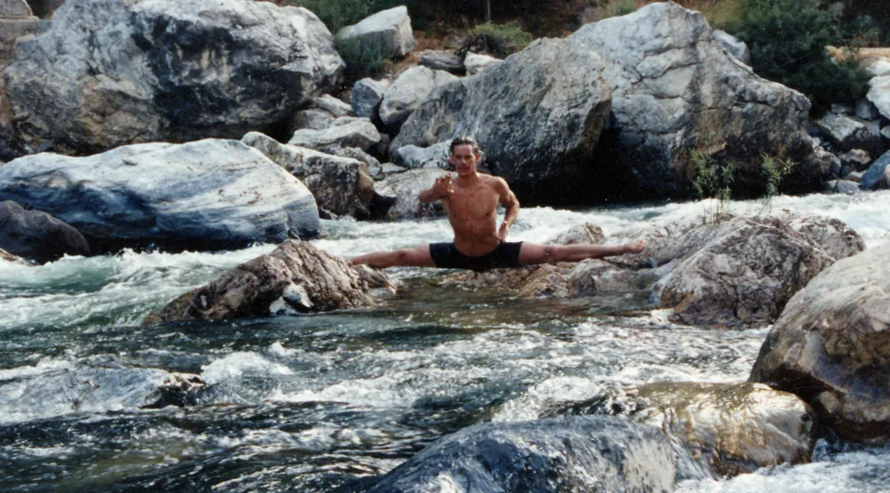 Rick Tew in the splits on rocks in a mountain river