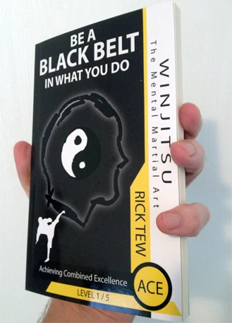A hand holding the WinJitsu book Achieving Combined Excellence by Rick Tew